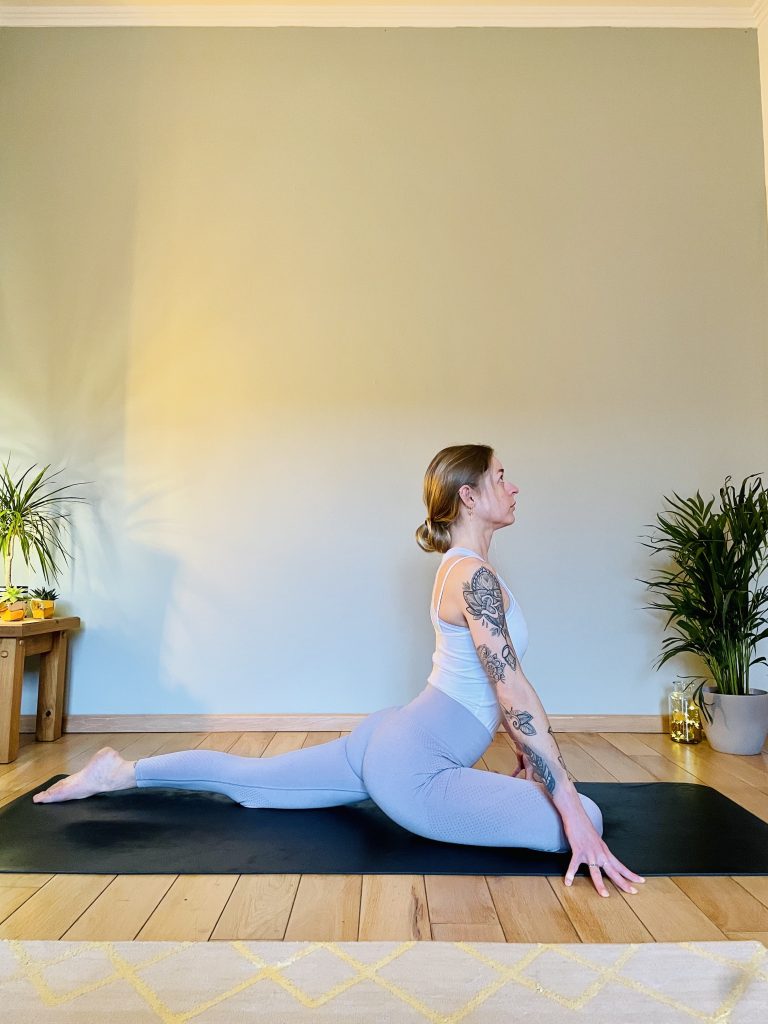 Image depicting a woman practicing the yoga pose "pigeon" viewed from the side in the starting position - a great yoga pose for opening the hips.