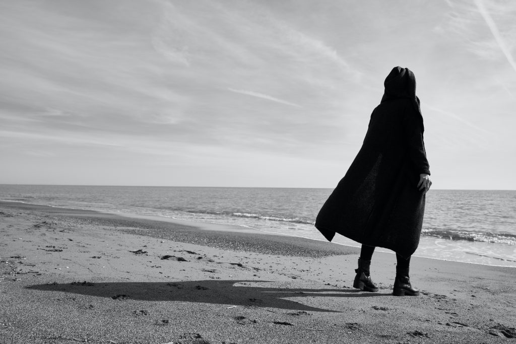 Image showing a woman on the beach dressed in black, embodying depression. Depression is not just an illness of the mind.