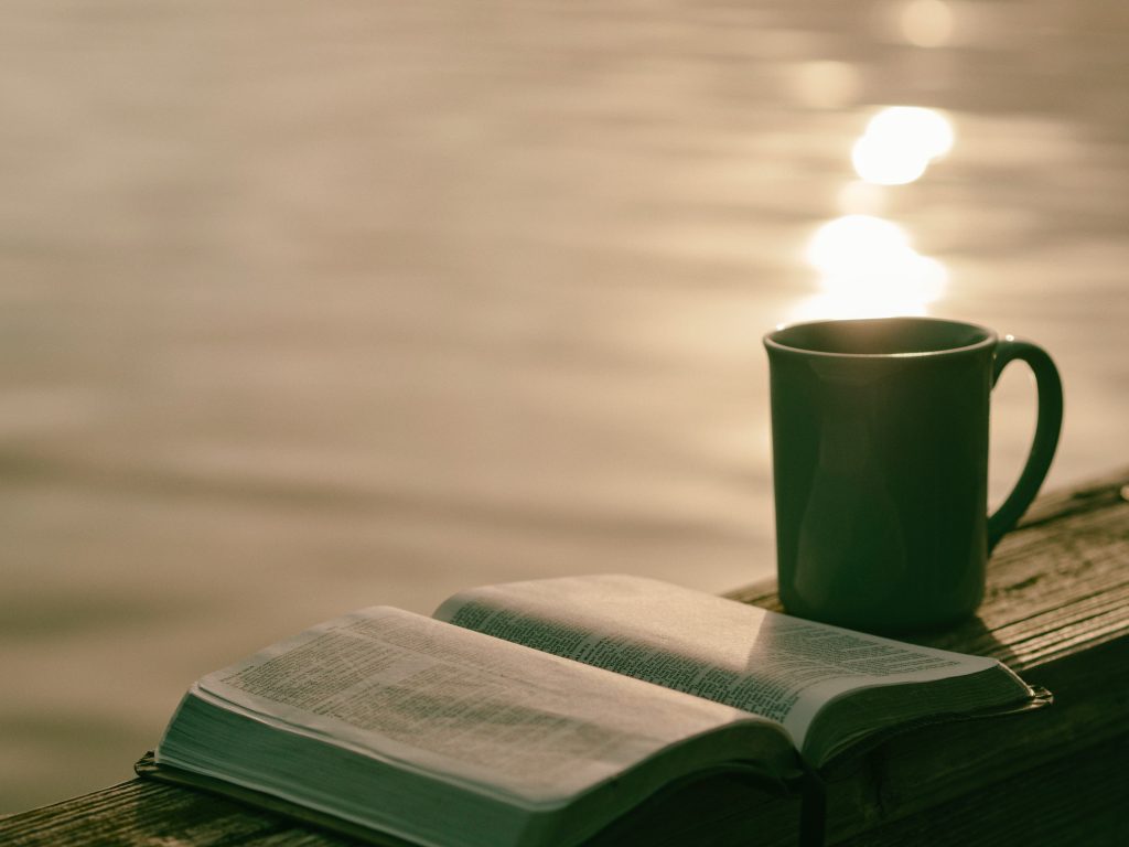 Image shows an open book with a tea mug next to it by a lake or ocean. One benefit of meditation is enhanced concentration.