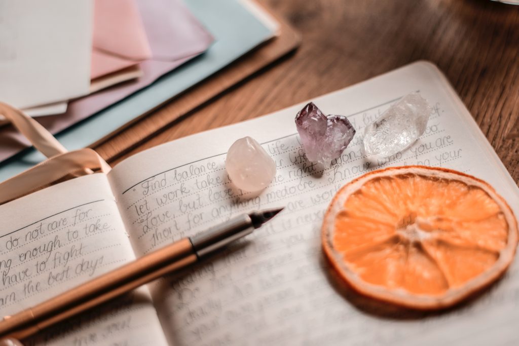 Image showing a handwritten journal with a pen and crystals. Gratitude journaling has been shown as an effective way of how to get better quality sleep.