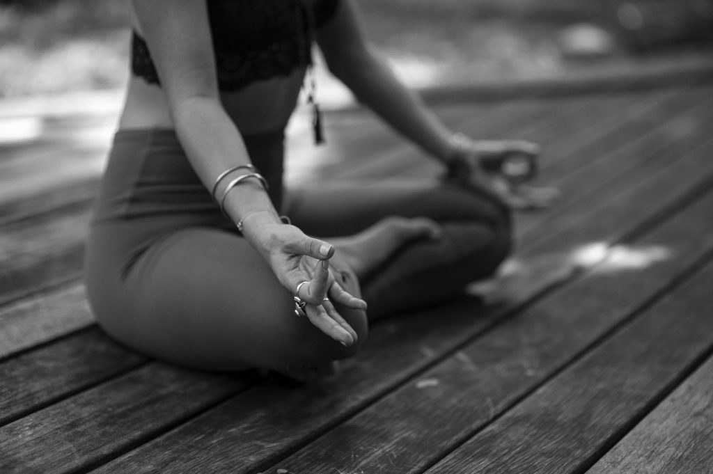 Image in black and white showing a girl in a cross-legged seat, meditating. Meditation can be a great mindfulness practice for newbies.