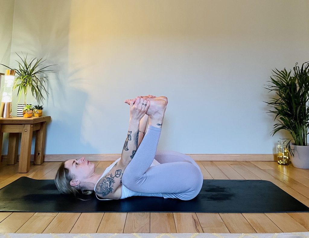 Girl practicing the hip opening yoga pose "ananda balasana" or happy baby, which is great for easing up lower back pain.