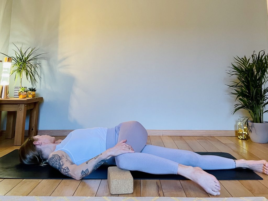 Image showing a girl practicing the yoga pose reclined twist. Twists bring mobility to the spine and can help to lessen lower back pain.