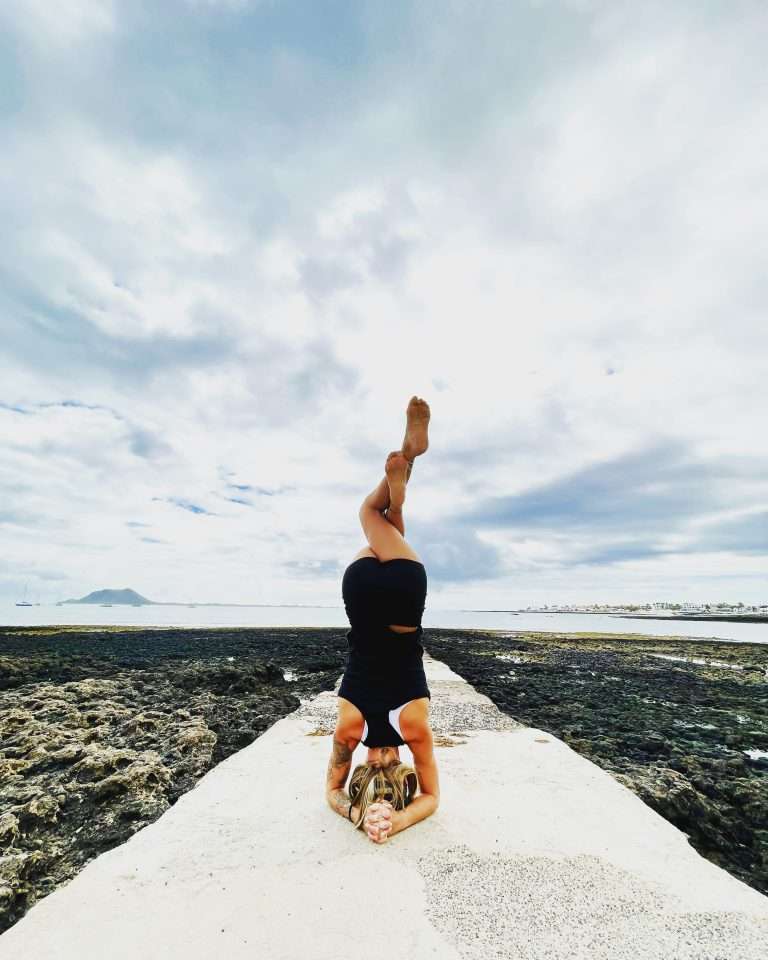 Girl practicing the yoga pose sirsasana, headstand, on a beach.