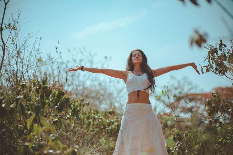 Woman standing outside in a field with the eyes closed and arms open sideways. Yoga for stress relief through asana, pranayama, and meditation. Yoga offers a great and holistic approach to stress relief.